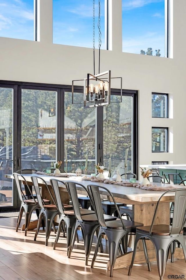 dining area featuring a healthy amount of sunlight, hardwood / wood-style floors, a chandelier, and a towering ceiling