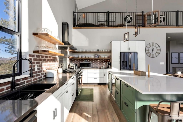 kitchen with white cabinetry, sink, green cabinetry, stainless steel appliances, and wall chimney range hood