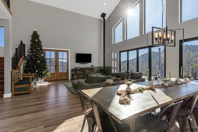 dining space featuring french doors, high vaulted ceiling, a wood stove, a notable chandelier, and hardwood / wood-style flooring