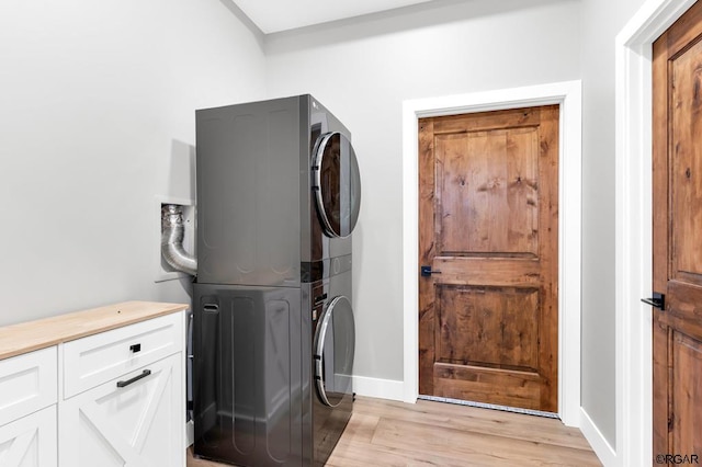 laundry area with stacked washer / drying machine, light hardwood / wood-style floors, and cabinets