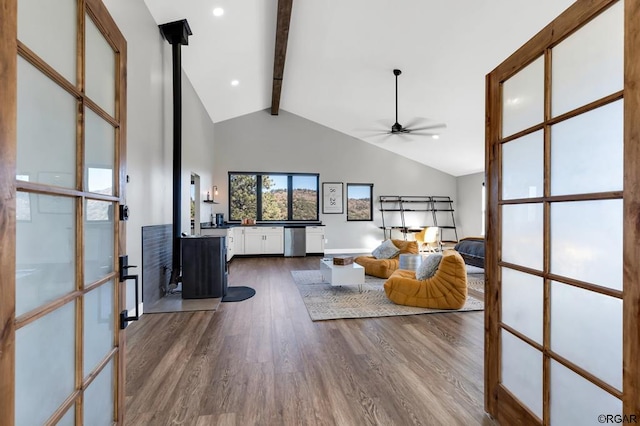 living room featuring hardwood / wood-style floors, high vaulted ceiling, a wood stove, ceiling fan, and beam ceiling