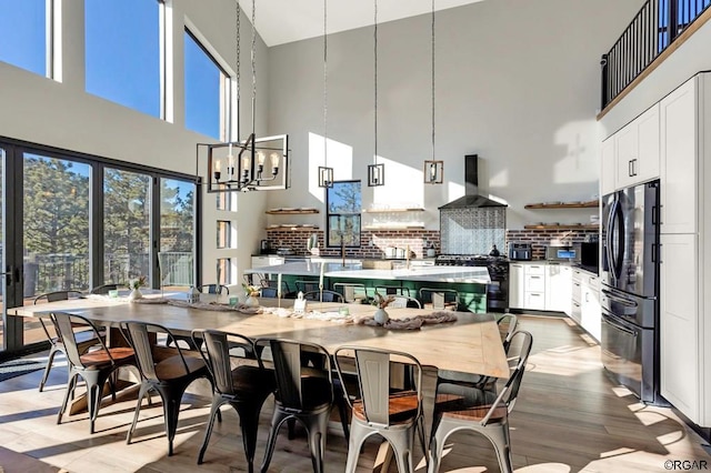 kitchen featuring white cabinetry, hanging light fixtures, stainless steel refrigerator, wall chimney range hood, and a high ceiling