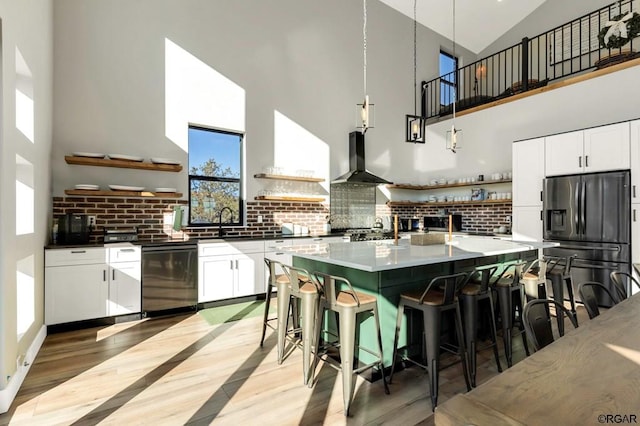 kitchen featuring high vaulted ceiling, dishwasher, refrigerator with ice dispenser, and wall chimney range hood