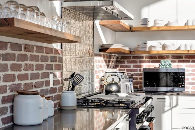 kitchen featuring stainless steel appliances, brick wall, exhaust hood, and white cabinets