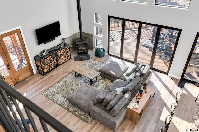 living room featuring a towering ceiling, a wood stove, and light wood-type flooring