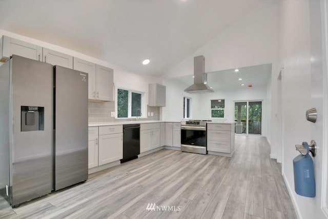 kitchen featuring appliances with stainless steel finishes, wall chimney range hood, backsplash, high vaulted ceiling, and light hardwood / wood-style flooring