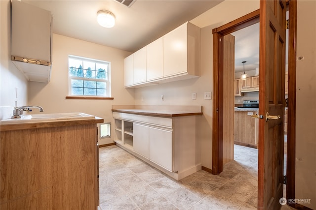 kitchen with stove, white cabinets, sink, and light tile flooring