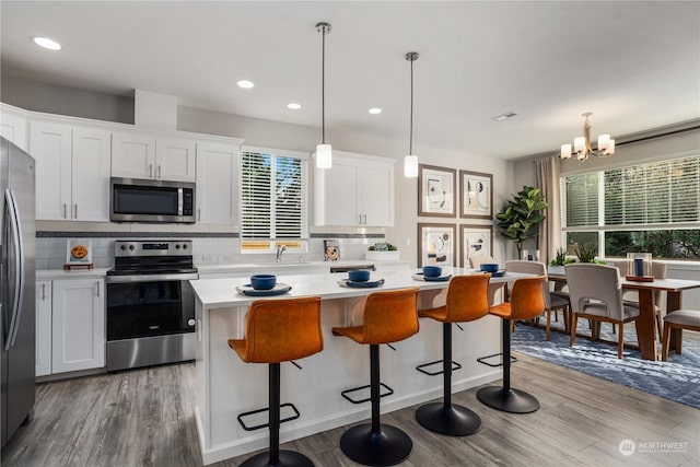 kitchen with decorative light fixtures, white cabinetry, a center island, light hardwood / wood-style floors, and stainless steel appliances