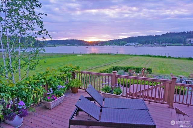 deck at dusk with a water view and a yard