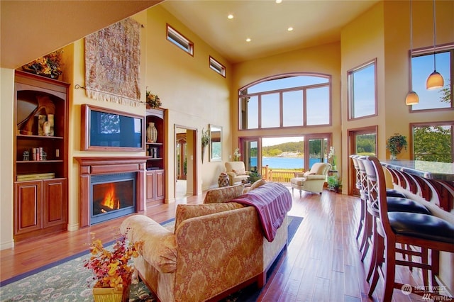 living room featuring a water view, light hardwood / wood-style flooring, and a towering ceiling