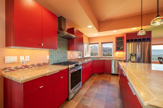 kitchen with hanging light fixtures, wall chimney range hood, stainless steel appliances, backsplash, and dark tile flooring