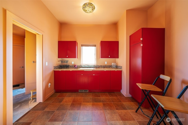 kitchen featuring dark tile floors, sink, and light stone counters