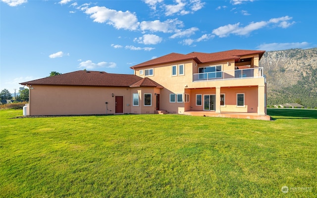 rear view of house with a lawn, a balcony, and a patio area