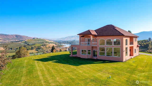 rear view of property featuring a balcony, a lawn, and a mountain view