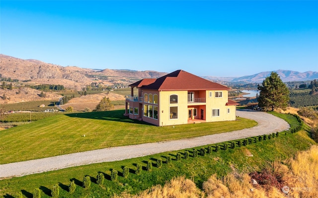 view of front of house featuring a balcony, a front yard, a mountain view, and a rural view