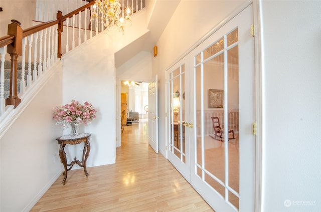 corridor featuring a notable chandelier, light hardwood / wood-style flooring, french doors, and a towering ceiling