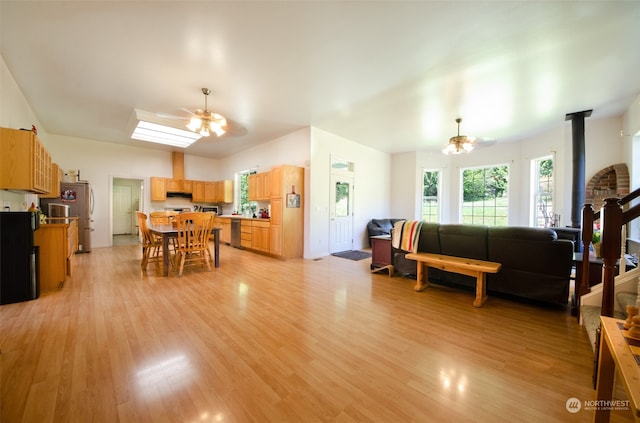 living room with brick wall, a wood stove, ceiling fan, and light wood-type flooring