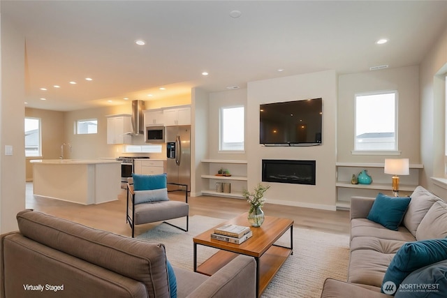 living area featuring recessed lighting, visible vents, baseboards, light wood-type flooring, and a glass covered fireplace