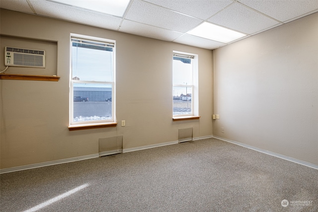 empty room featuring a drop ceiling, carpet, and a wall mounted air conditioner