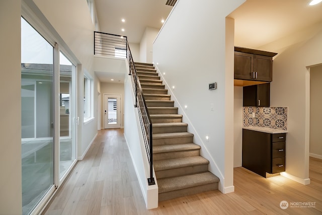 stairway with recessed lighting, a towering ceiling, baseboards, and wood finished floors