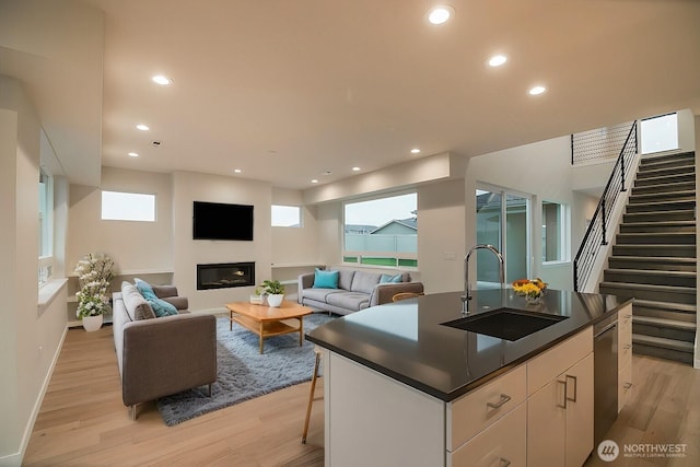 kitchen featuring dark countertops, light wood-type flooring, a sink, and a glass covered fireplace