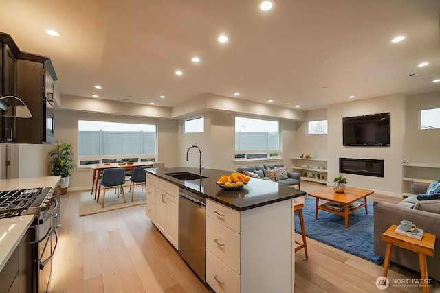 kitchen featuring stainless steel appliances, a sink, light wood-style floors, open floor plan, and dark countertops