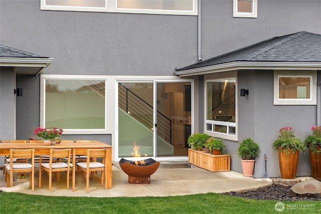 rear view of house featuring outdoor dining space, roof with shingles, a patio area, and stucco siding