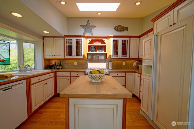 kitchen featuring a kitchen island, wooden counters, a skylight, white dishwasher, and a sink