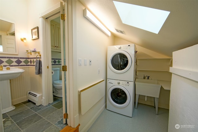 laundry area featuring laundry area, a wainscoted wall, a skylight, a baseboard heating unit, and stacked washing maching and dryer
