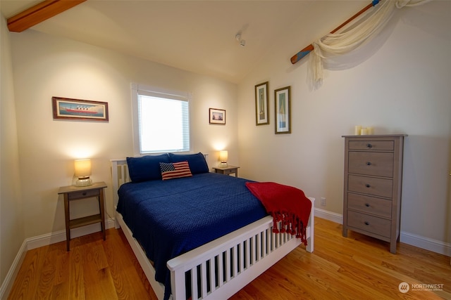 bedroom with baseboards, light wood-type flooring, and vaulted ceiling