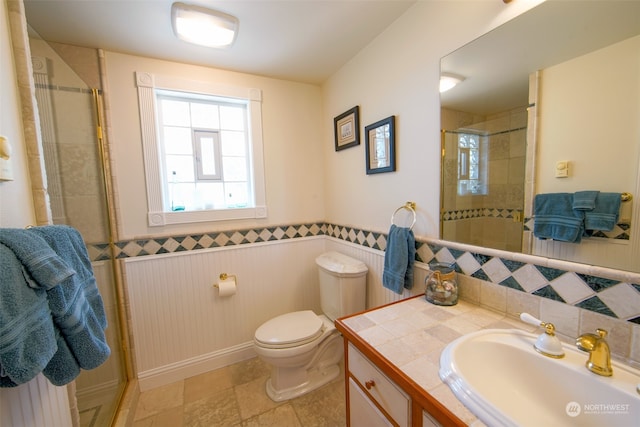 full bath featuring toilet, vanity, wainscoting, and a stall shower