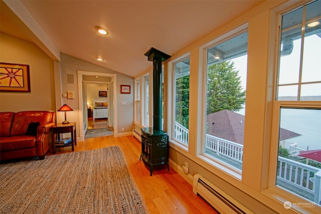 living area with light wood-type flooring, a baseboard heating unit, vaulted ceiling, and a wood stove
