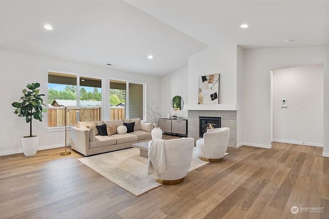 living room featuring a tiled fireplace, light wood-type flooring, and vaulted ceiling