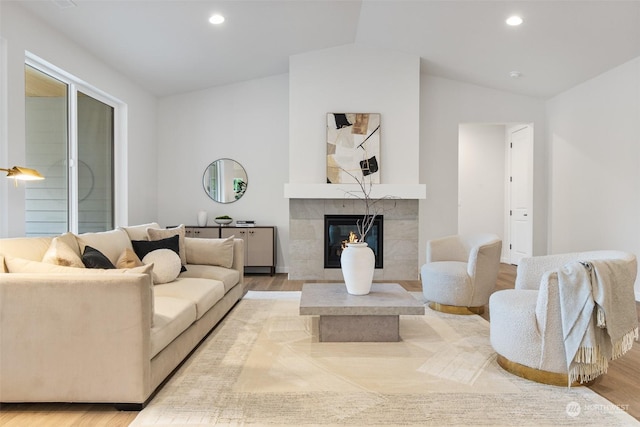 living room with light wood-type flooring, lofted ceiling, and a tiled fireplace