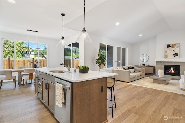 kitchen featuring stainless steel dishwasher, sink, decorative light fixtures, a center island with sink, and light hardwood / wood-style floors