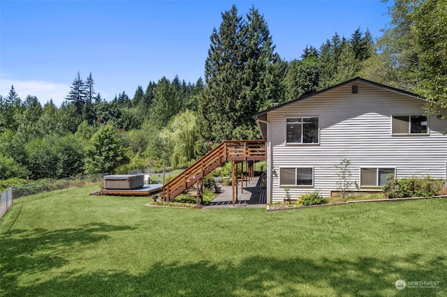 rear view of property featuring a wooden deck, a hot tub, and a lawn