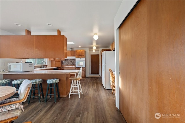 kitchen featuring a kitchen breakfast bar, kitchen peninsula, white appliances, and dark hardwood / wood-style floors