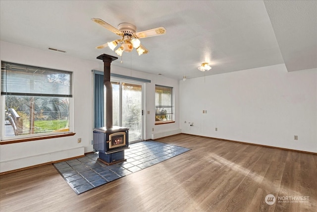 unfurnished living room featuring ceiling fan, a wood stove, and dark hardwood / wood-style flooring