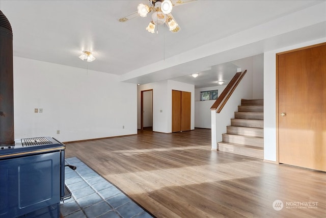 unfurnished living room with ceiling fan, a wood stove, and wood-type flooring