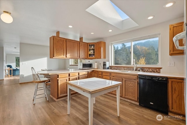 kitchen with black dishwasher, sink, a skylight, and light hardwood / wood-style flooring