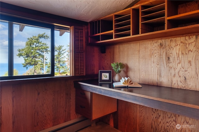 unfurnished office featuring a water view, a baseboard radiator, wooden walls, and a textured ceiling