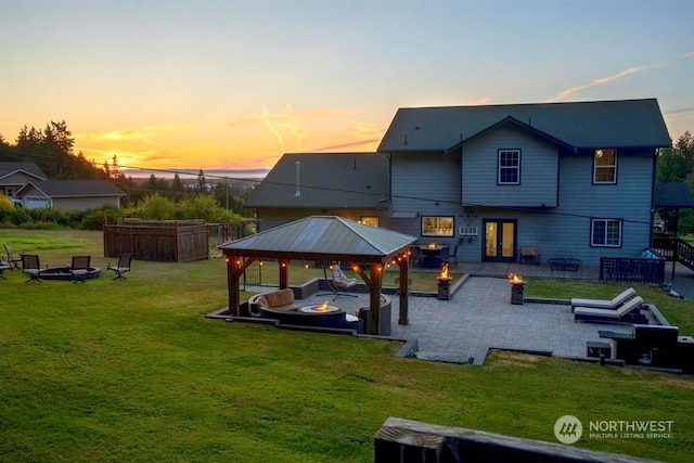 back house at dusk with a fire pit, a gazebo, a patio area, and a lawn