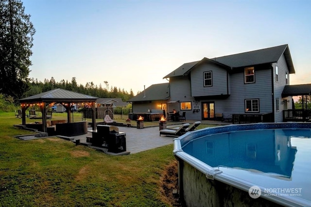 pool at dusk with a yard, a gazebo, an outdoor living space with a fire pit, and a patio