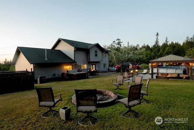 yard at dusk with an outdoor fire pit, a hot tub, a gazebo, and a patio