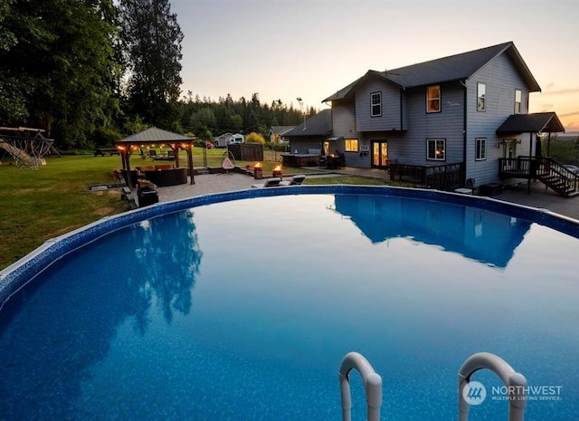 pool at dusk featuring a lawn, a patio, and a gazebo