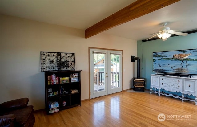 living room featuring beam ceiling, ceiling fan, a wood stove, and light wood-type flooring