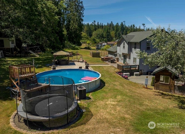 view of swimming pool featuring a deck, a lawn, a gazebo, and a trampoline