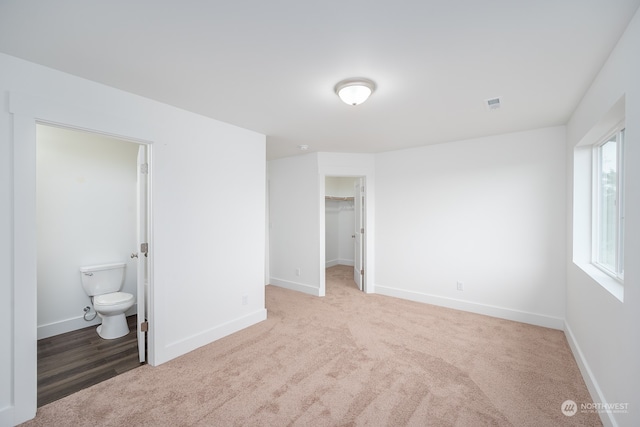 unfurnished bedroom with a closet, a spacious closet, ensuite bath, and light colored carpet