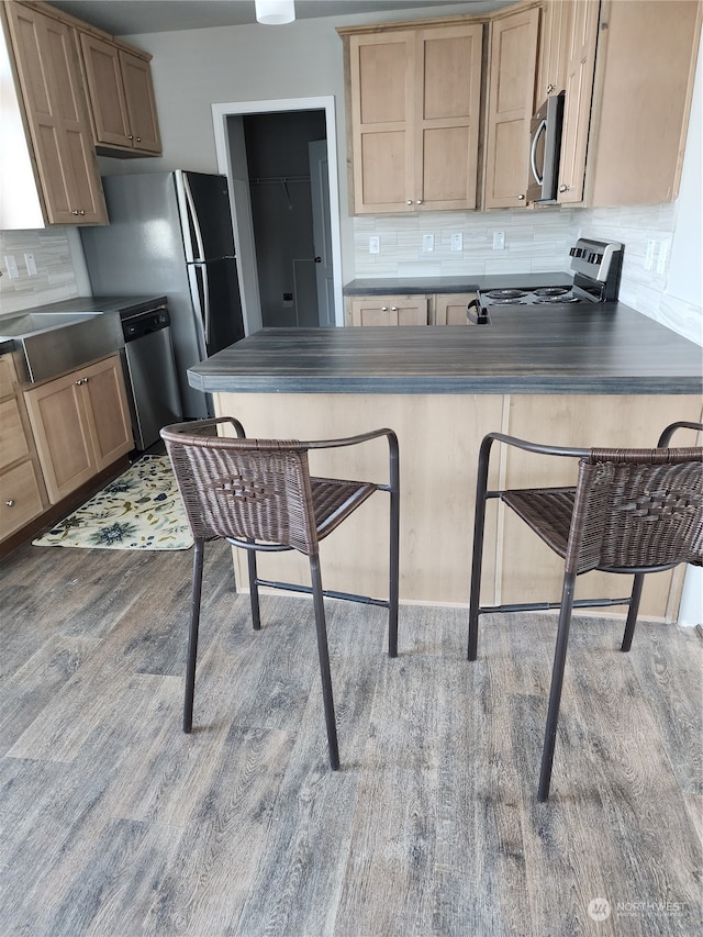 kitchen featuring appliances with stainless steel finishes, dark countertops, decorative backsplash, and wood finished floors