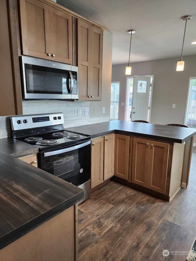 kitchen with dark wood-style floors, stainless steel appliances, dark countertops, tasteful backsplash, and a peninsula